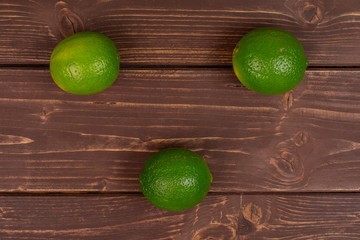 Group of three whole fresh green lime flatlay on brown wood