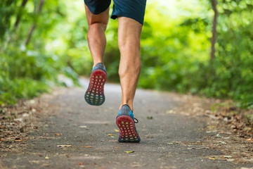 Runner man training marathon run race running on forest park city path outdoors from behind sprinting fast. Closeup of shoes and calves.