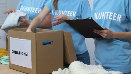 Wall Mural - Volunteers packing donated clothes in boxes, supervisor holding check list, care