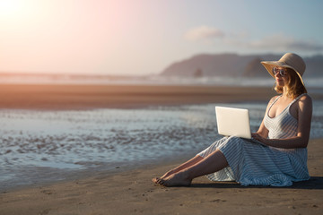 Wall Mural - Young girl in sunglasses works on a laptop on the ocean at sunset, freelancing, making money on the Internet, getting money online, lifestyle, Banne, with space