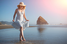 A Girl In A Hat At Sunset Near The Ocean Splashes Water With Splashes. A Woman's Style And Fashion, Relaxing On The Beach, Walking, With Space