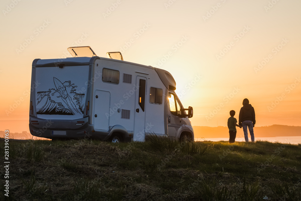 mother and son watching the sunset with their motor home at the edge of the sea - obrazy, fototapety, plakaty 