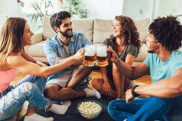 Wall Mural - Friends eating popcorn and drinking beer mug at home, having fun.