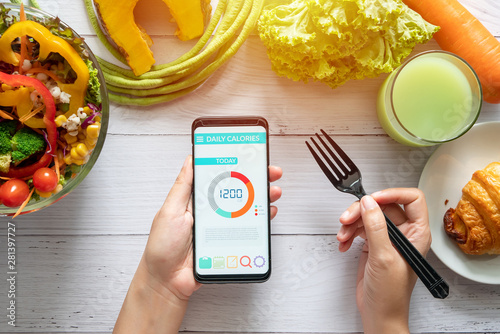 Calories counting , diet , food control and weight loss concept. woman using Calorie counter application on her smartphone at dining table with salad, fruit juice, bread and vegetable