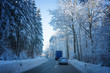 PKW fährt dicht hinter einem LKW auf winterlicher Straße durch den Wald. Wartet auf Gelegenheit zum Überholen.