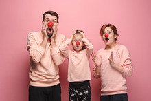 Portrait Of Young Family Celebrating Red Nose Day. Male And Female Models Looks Crazy Happy, Astonished, Surprised On Coral Studio Background. Victory, Delight Concept. Human Facial Emotions.