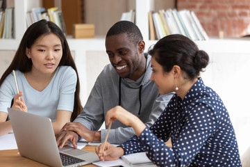 Smiling diverse students talk working on laptop together