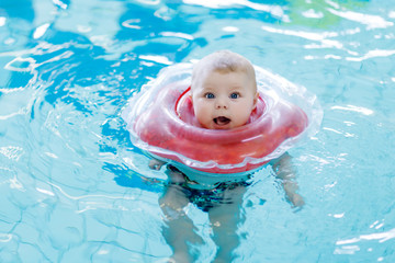 Wall Mural - Cute little baby child learning to swim with swimming ring in an indoor pool