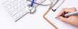 © RomixImage - Female doctor writing a medical record case over clipboard on white working table with stethoscope, computer keyboard. Top view, flat lay, copy space