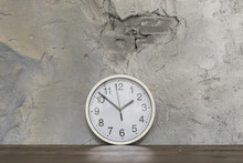 Round Clock Face Leaning Against Damaged Concrete Wall On Wooden Desk