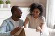 © fizkes - African couple unpack carton box sitting on sofa feels happy
