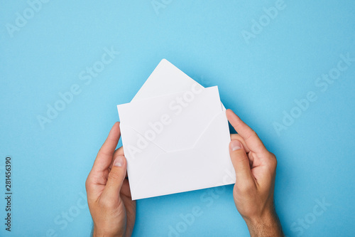 Cuadros en Lienzo cropped view of man holding envelope with blank white card on blue background