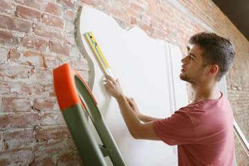 Young man preparing for doing apartment repair by hisselfes. Before home makeover or renovation. Concept of relations, family, DIY. Measuring the wall before painting or design making.