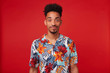 © timtimphoto - Young African American man wears in Hawaiian shirt, looks at the camera and calm smiling, stands over red background.