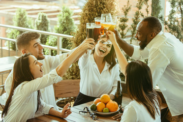 Young group of friends drinking beer, having fun, laughting and celebrating together. Women and men with beer's glasses in sunny day. Oktoberfest, friendship, togetherness, happiness, summer concept.