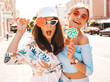 canvas print picture - Two young beautiful smiling hipster girls in trendy summer clothes and panama hat. Sexy carefree women posing on street background.Positive models having fun in sunglasses.Eating candy lollipop