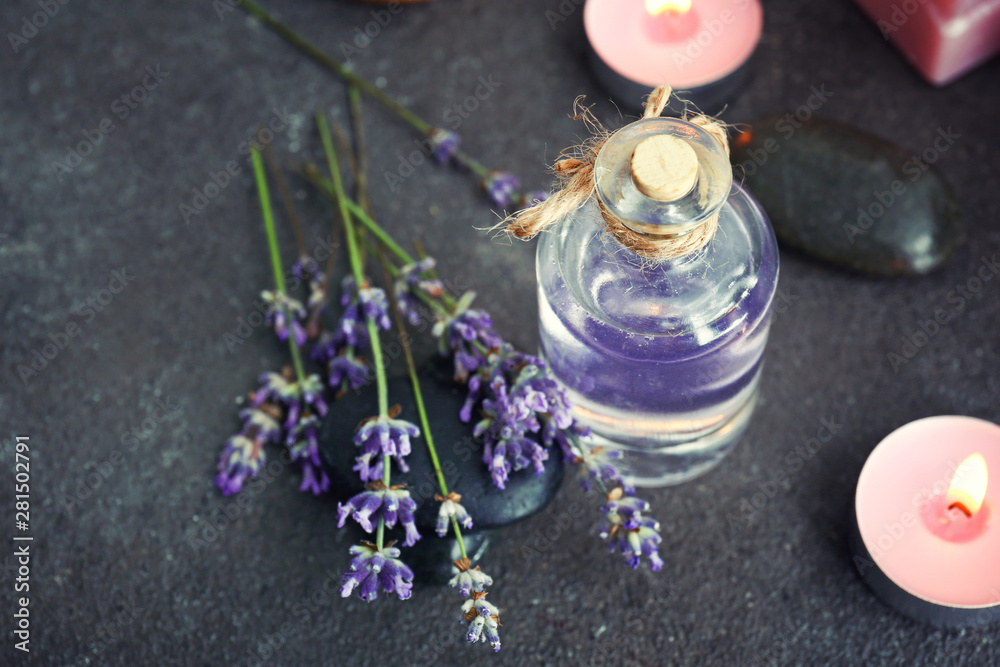 Bottle of lavender essential oil and candles on grey table
