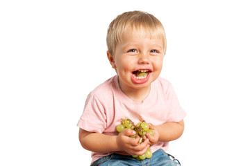 Baby boy eating grapes and smiling in the studio isolated on white background. Concept healthy food