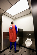 Rear View Of Businessman In Super Hero Costume Standing In Public Toilet