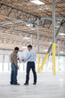© Mint Images - Architects talking over blueprint while standing in warehouse