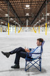 © Mint Images - Man using smartphone while sitting on chair in warehouse