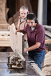 © Mint Images - Carpenters cutting large wooden slab on table saw in workshop