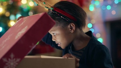 happy african american girl unwrapping christmas present looking in box with glow on face surprised 