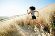 © Mint Images - Rear view of young woman running in grassy field