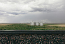 Stormy Clouds Over Grain Silos On Farmland With Rail Track In Foreground