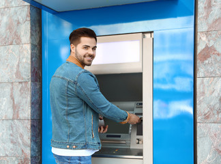 Young man using modern cash machine outdoors