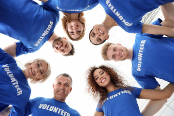 Wall Mural - Team of volunteers joined in circle on light background, bottom view