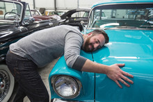 Smiling Mechanic Hugging Hood Of Car In Automobile Repair Shop
