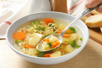 Woman eating fresh homemade vegetable soup at wooden table, closeup