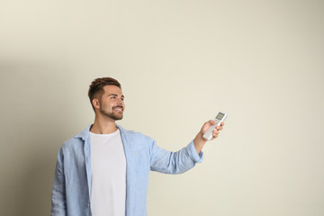 Canvas Print - Happy young man operating air conditioner with remote control on beige background. Space for text