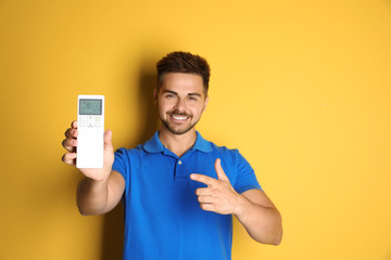 Wall Mural - Happy young man with air conditioner remote control on yellow background