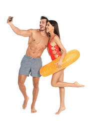 Poster - Young attractive couple in beachwear with inflatable ring taking selfie on white background