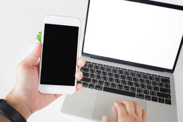 Poster - Laptops and hands are holding a smartphone with a blank screen on a white table inside the home or office. Isolated on white.