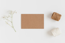 Top View Of A Kraft Card Mockup With A Gypsophila And Workspace Accessories On A White Table.