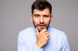 © F8  \ Suport Ukraine - Young handsome man with hand on chin thinking about question, pensive expression over isolated gray background. Smiling with thoughtful face. Doubt concept.