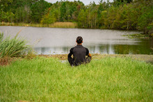 A Man Sits On The Ground In Meditation Overlooking A Beautiful Lake In Orlando, Florida.