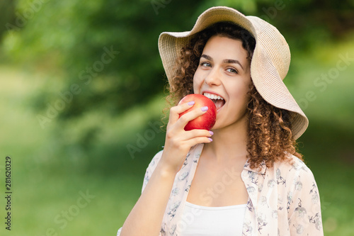Fotomural Beautiful girl in a hat eats an apple on nature