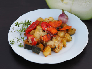 Beautiful vegetable stew with courgettes, tomatoes, peppers, carrots and grilled cheese baked are in a white plate on a wooden table close-up. Appetizing and healthy vegetable food.