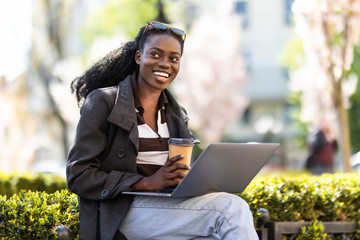 Wall Mural - Happy young relaxed african girl using a laptop in the street