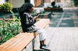 © F8  \ Suport Ukraine - Portrait of happy young african woman sitting outside on bench reading a text message on her mobile phone