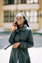 Wall Mural - Portrait of young african american girl talking by mobile phone, smiling. Sunny day. Outdoor photo.