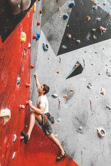 Wall Mural - Sportsman climber moving up on steep rock, climbing on artificial wall indoors. Extreme sports and bouldering concept