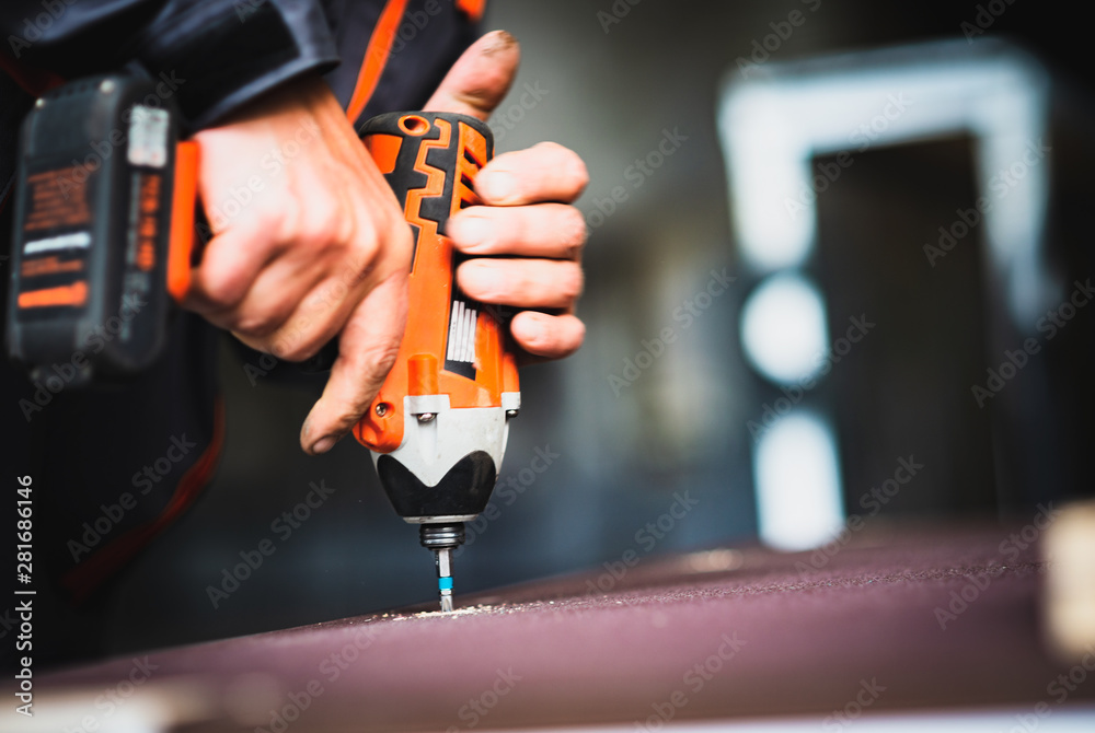 Worker tightens a screw with an electric screwdriver - obrazy, fototapety, plakaty 