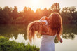 © maryviolet - Mother playing and having fun with daughter by summer river at sunset. Woman holding kid and laughing. Family