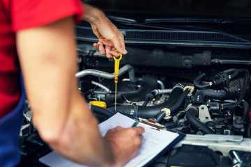 Wall Mural - car inspection and maintenance - mechanic check engine oil level and writing in checklist