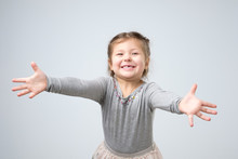 Studio Shot Of A Friendly Cute Female Toddler Stretching Hands Towards The Camera, Smiling From Happiness. Give Me A Warm Hug.